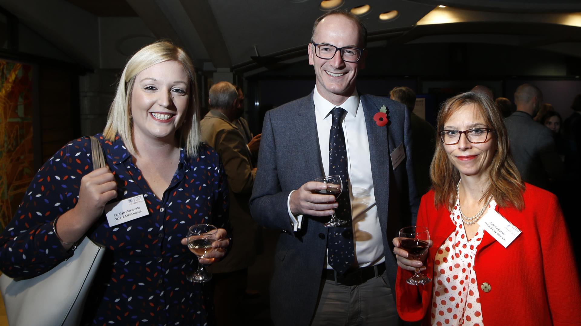 Three people standing, holding a glass of wine at the OPT awards