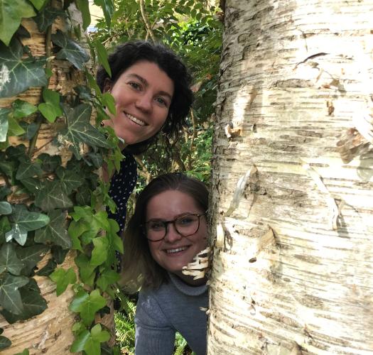 two people peeking out from behind a tree