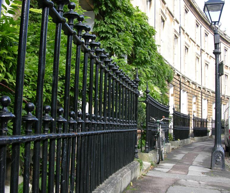 An image of black cast-iron traditional railings against a backdrop of greenery