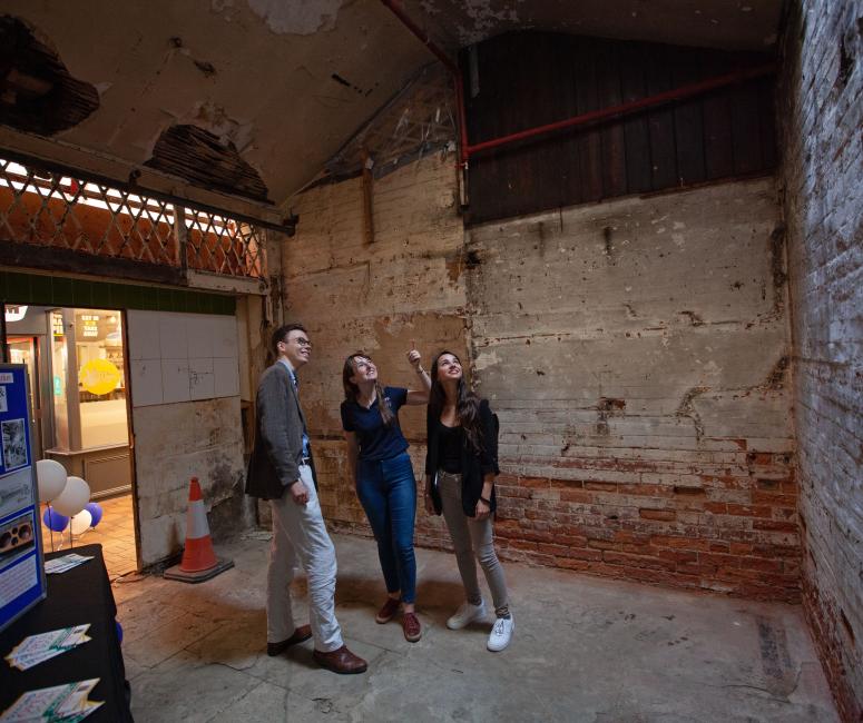 Three people standing in an empty unit, pointing towards the ceiling