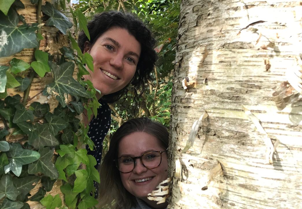 two people peeking out from behind a tree